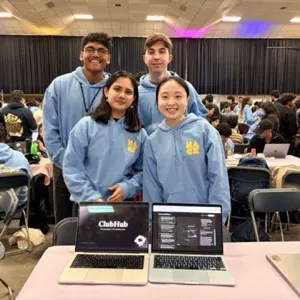 The ClubHub team in HackMIT hoodies behind two laptops showing ClubHub