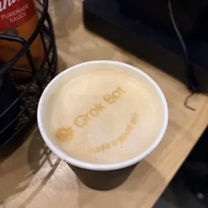 A latte with Grok Bot printed in the foam at HackMIT